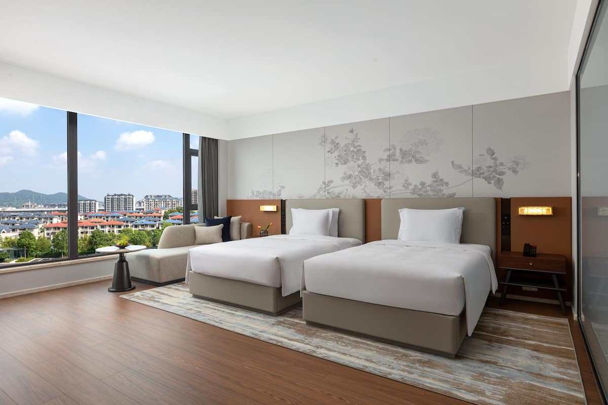 Une chambre d’hôtel moderne avec deux lits, une grande fenêtre donnant sur la ville et un panneau décoratif mural.