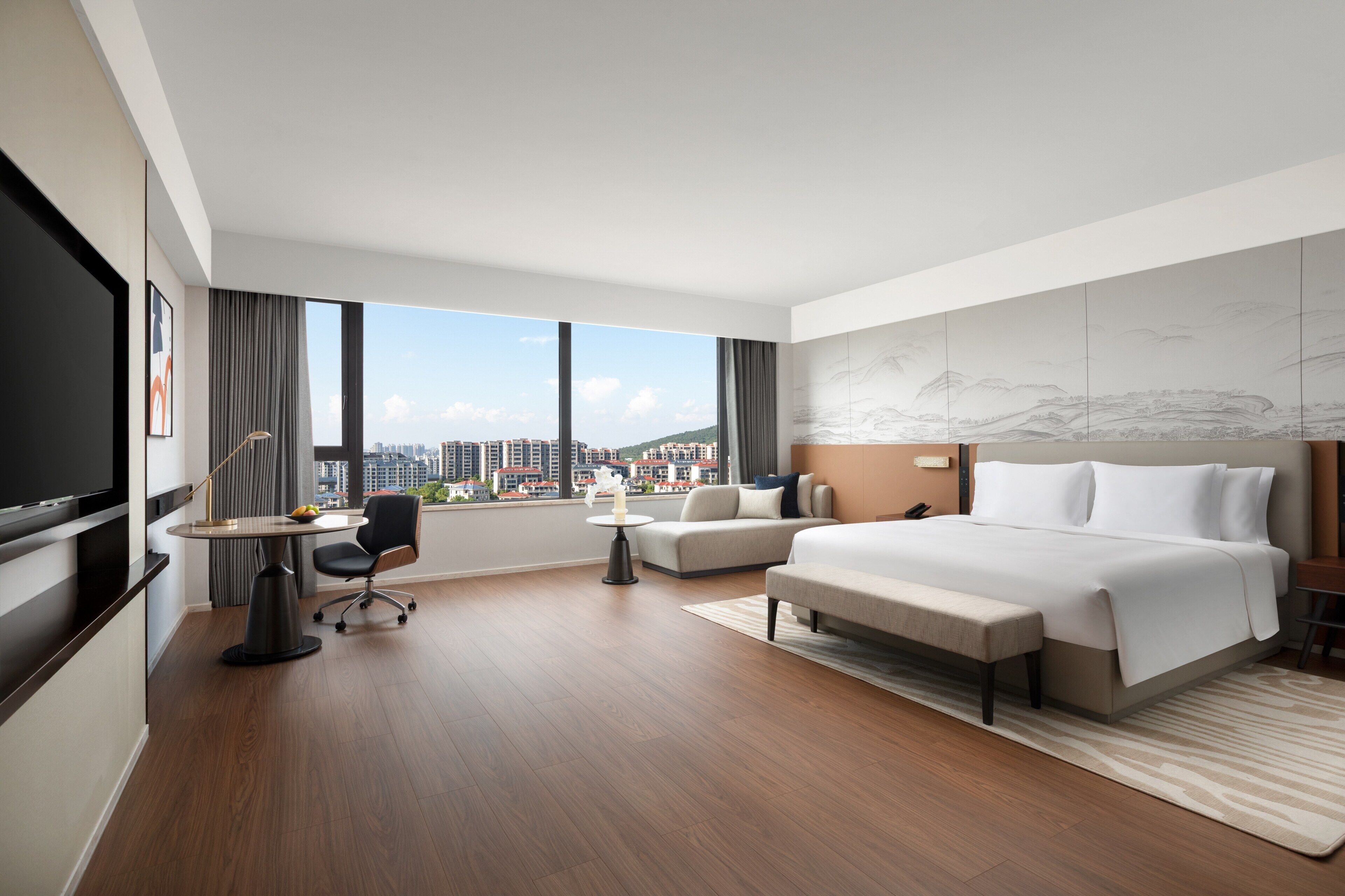 Ein modernes Hotelzimmer mit einem großen Bett, einem Schreibtisch mit Stuhl, einer Sitzecke und einem Fernseher.