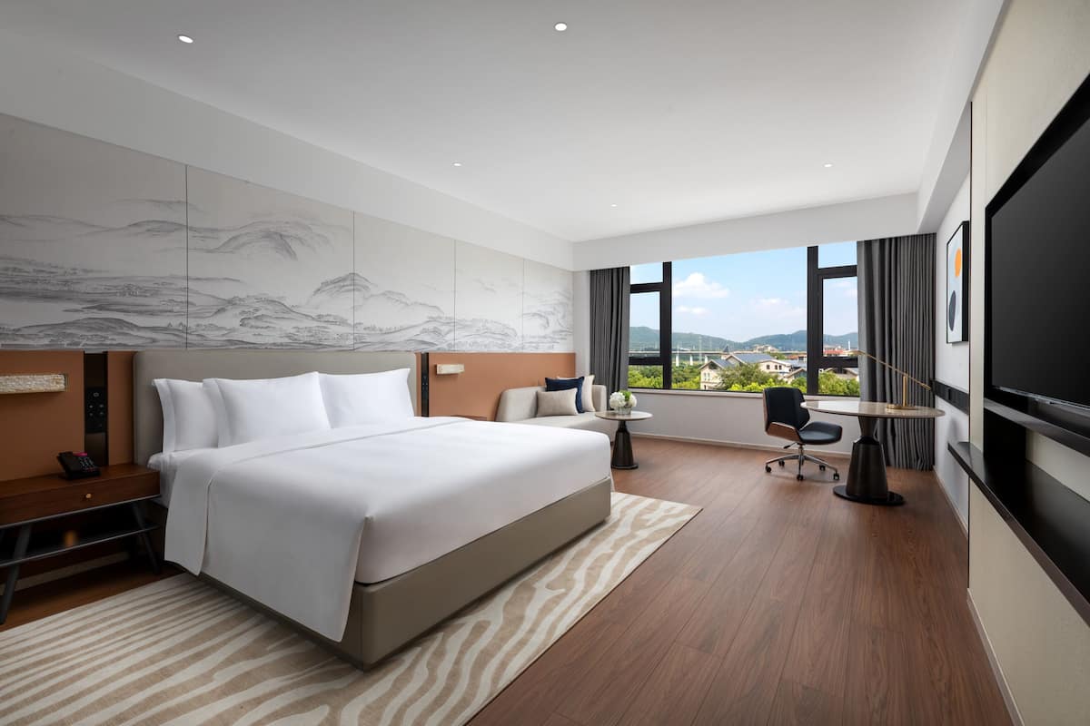 Une chambre d’hôtel moderne dotée d’un grand lit, d’un bureau, d’une chaise, d’une télévision et offrant une vue sur la ville.
