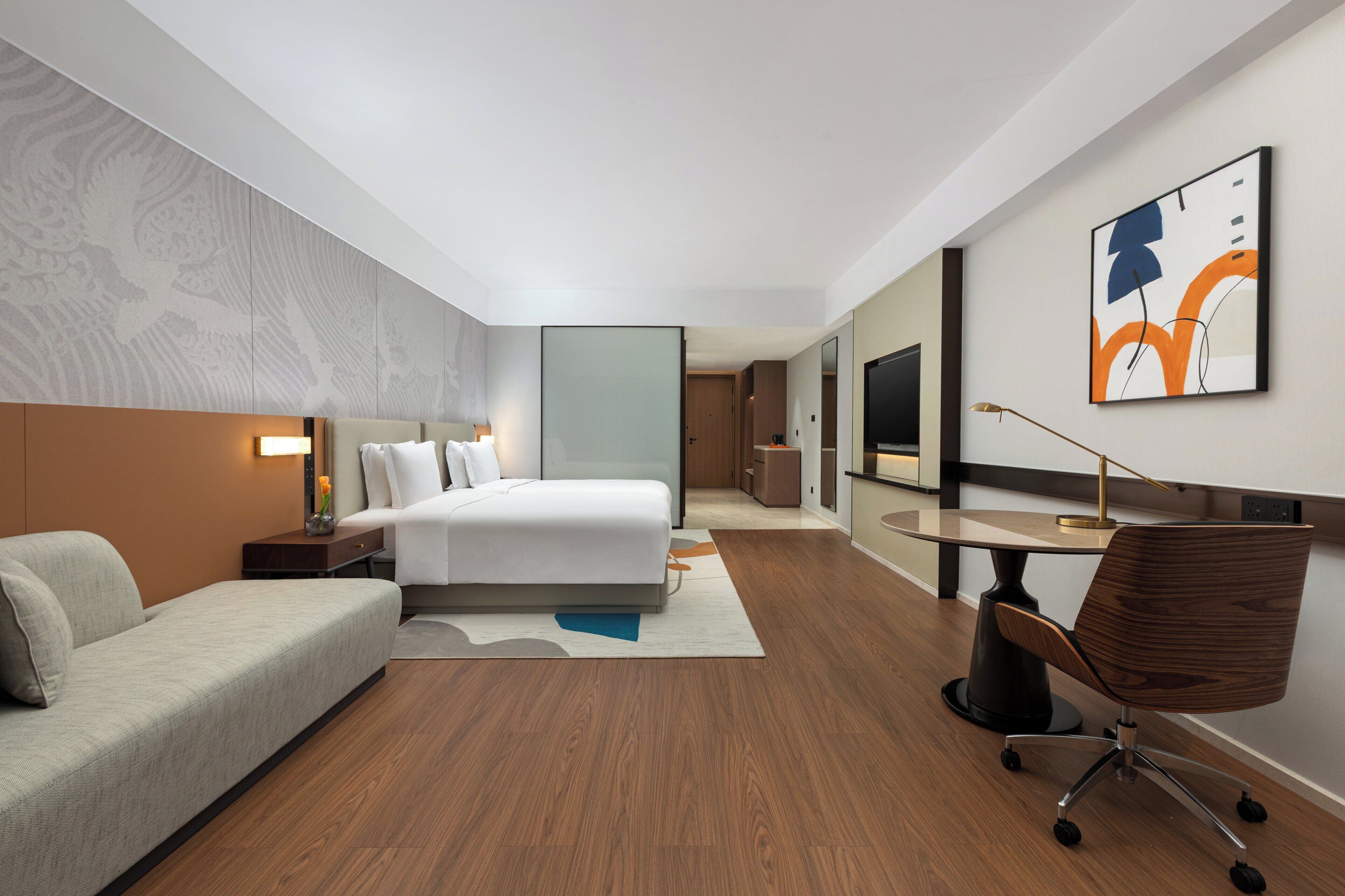 Una habitación de hotel moderna con cama, escritorio, sillón, sofá y televisor.