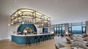 A modern bar area with a curved ceiling, bar stools, and a view of the city through large windows. - Crowne Plaza Xiangyang Fuchun Lakeside by IHG (Xiangyang)