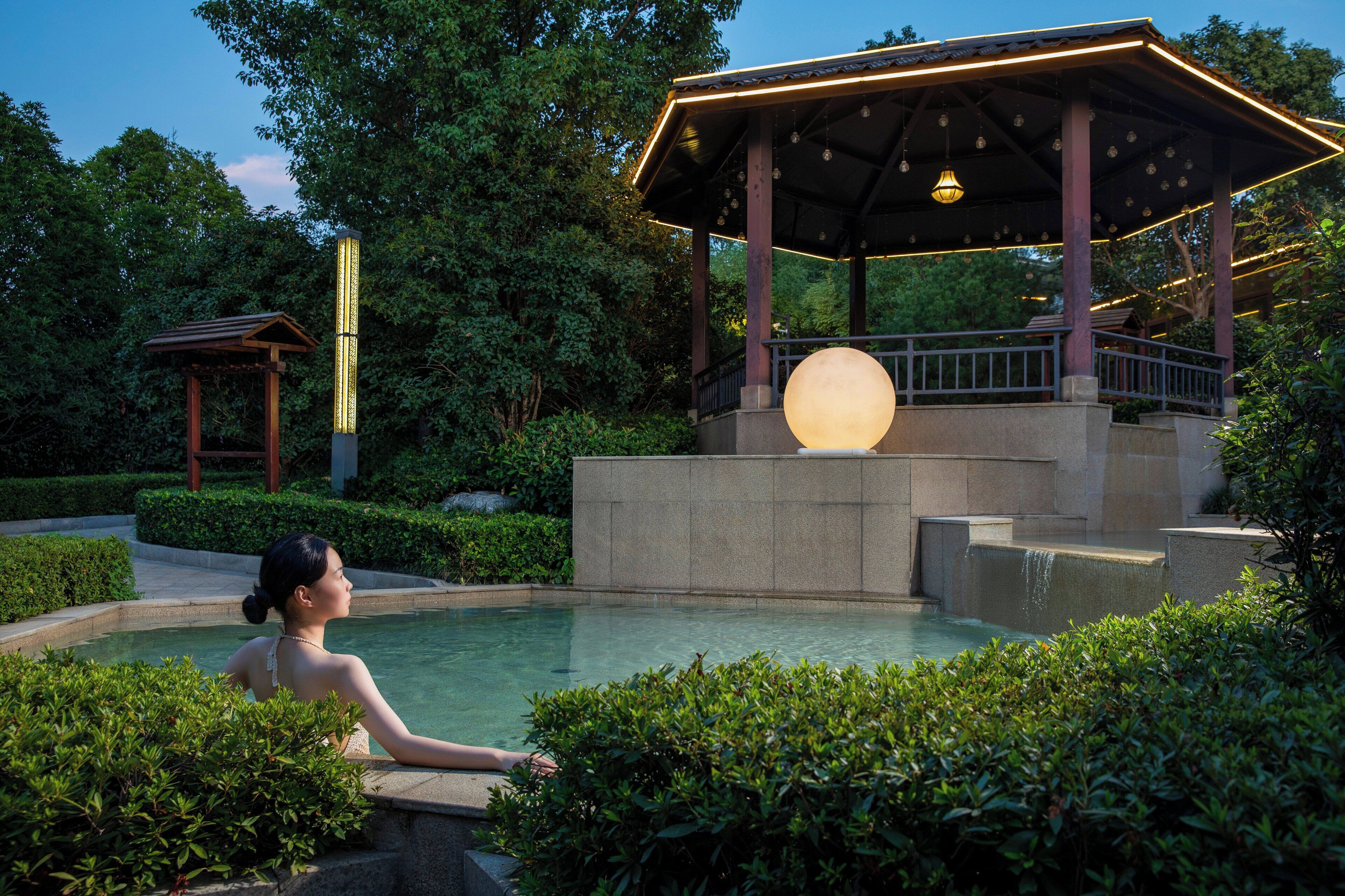 A serene outdoor pool area with a gazebo, a large illuminated sphere, and lush greenery.