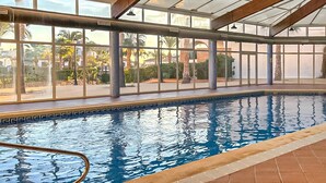 Une piscine intérieure avec des parois en verre transparent, un sol carrelé et un espace autour de la piscine agrémenté d’une rambarde.