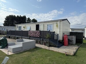 A mobile home with a fenced patio area, outdoor seating, and a small shed.