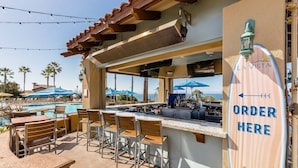 Un espace bar extérieur avec une piscine, des tabourets de bar et un panneau indiquant « Commandez ici ».
