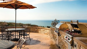 Une terrasse extérieure avec un mur en pierre, une table ronde et des chaises, offrant une vue panoramique sur la mer.