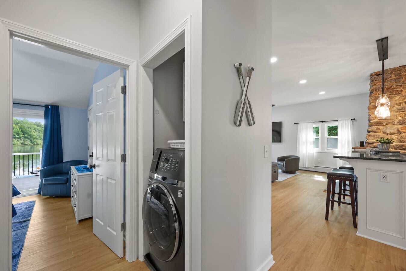A modern apartment with a laundry area, a kitchen with a stone accent wall, and a balcony with a view of greenery.