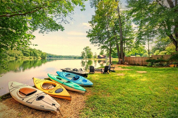 A lakeside setting with kayaks and chairs by the water.