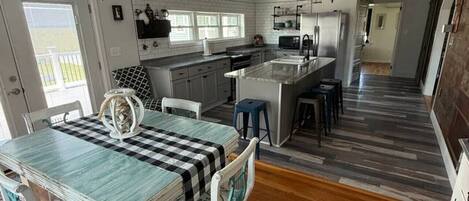 A spacious kitchen with a central island, wooden flooring, and a dining area with a checkered tablecloth.
