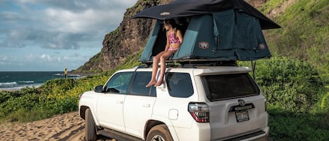 A white SUV parked on a sandy beach with a tent on top.