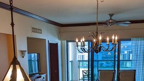 Une chambre d’hôtel dotée d’un coin cuisine, d’une table à manger, de chaises, d’un lustre et offrant une vue sur la ville grâce à de grandes fenêtres.