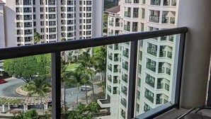 Un balcon avec une table ronde et des chaises, donnant sur un quartier résidentiel avec des immeubles à plusieurs étages et un ciel dégagé.