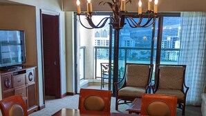 Une salle à manger d’hôtel avec une grande table en bois, six chaises, un lustre et une vue sur la ville grâce à de grandes fenêtres.