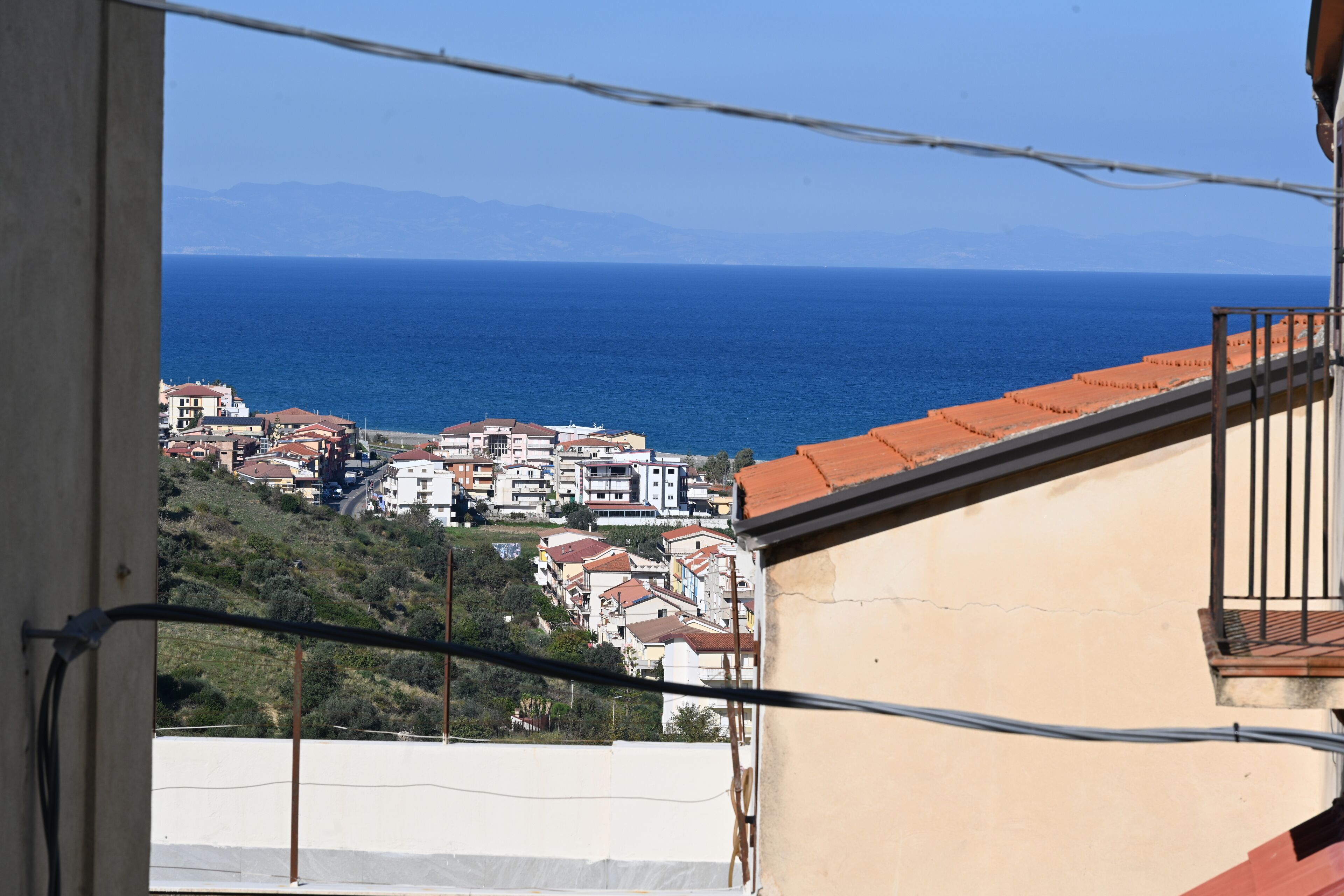 Vista da un balcone su una cittadina costiera con edifici e mare.