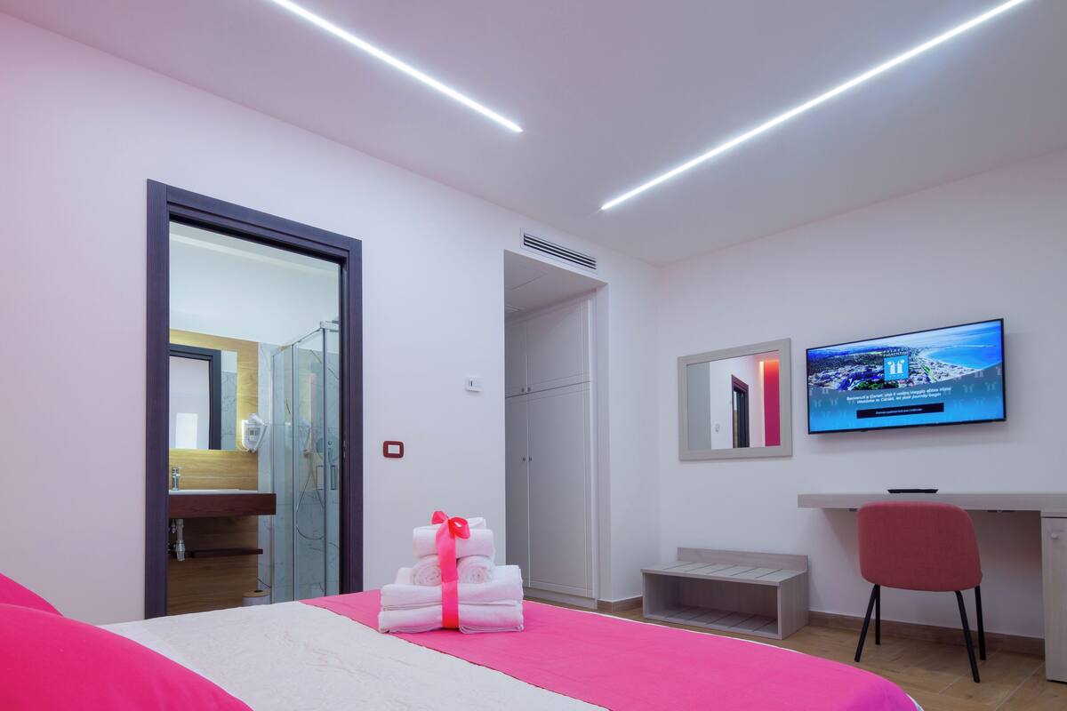 A modern hotel room with a bed, a desk, a TV, and a bathroom visible through an open door.