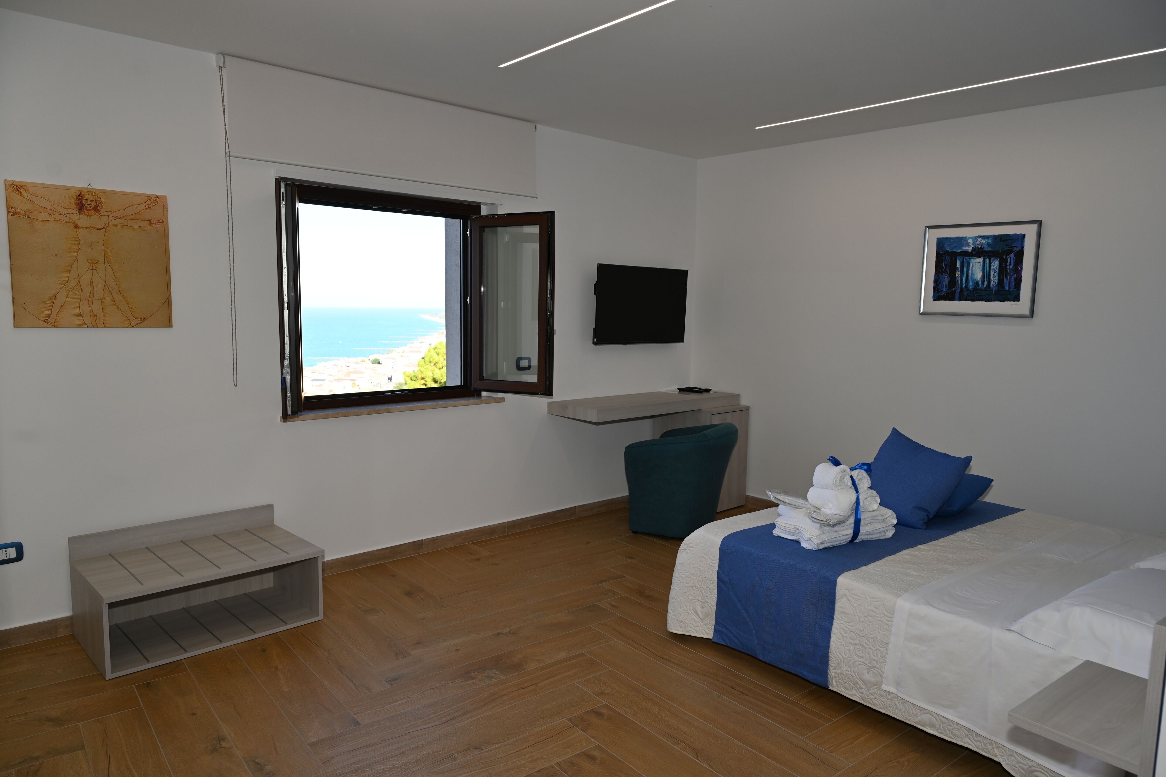 Ein modernes Hotelzimmer mit Bett, Schreibtisch, Stuhl, Fernseher und einem Fenster mit Meerblick.