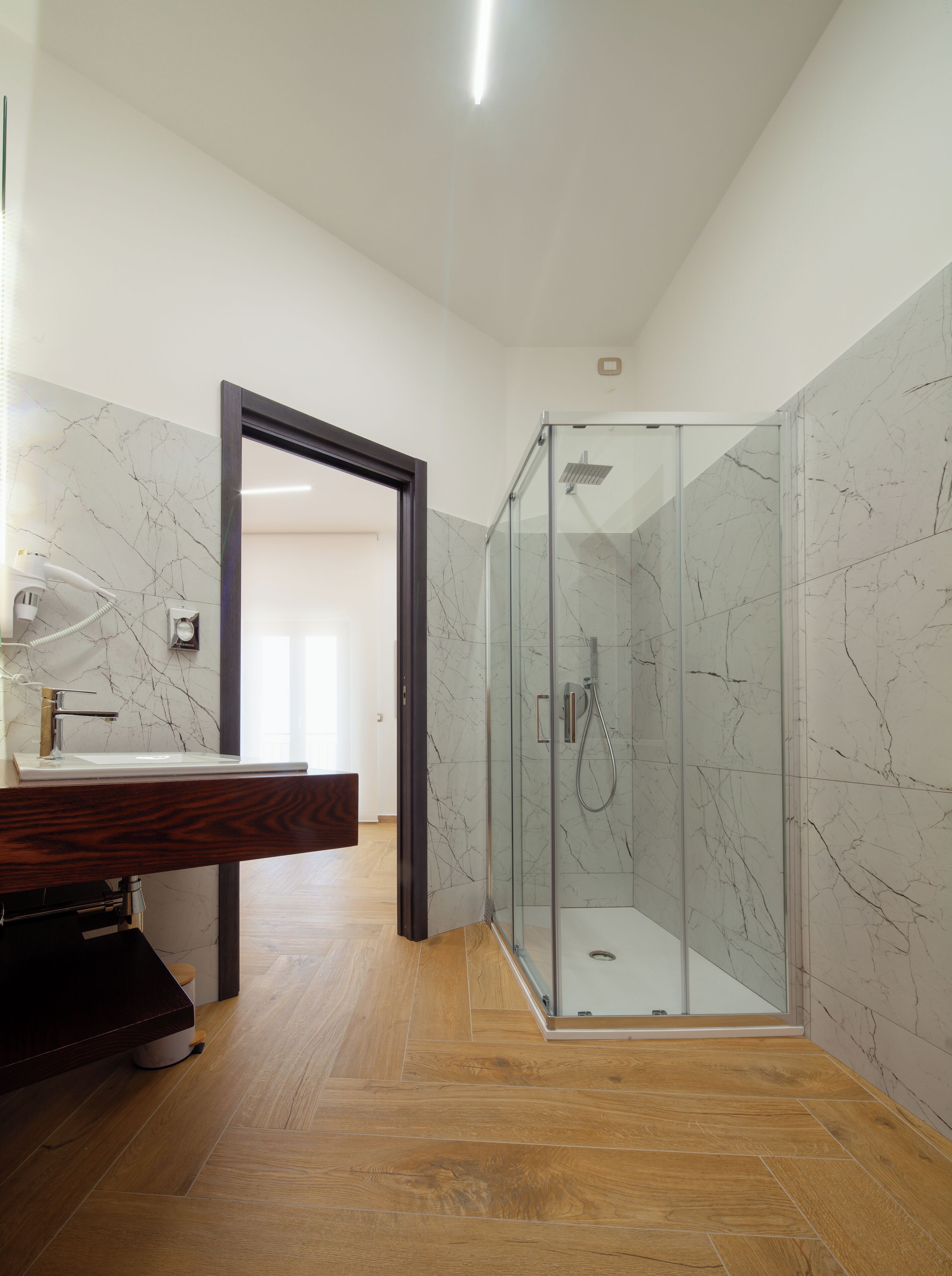 Un baño moderno con cabina de ducha de vidrio, paredes de mármol y tocador de madera.