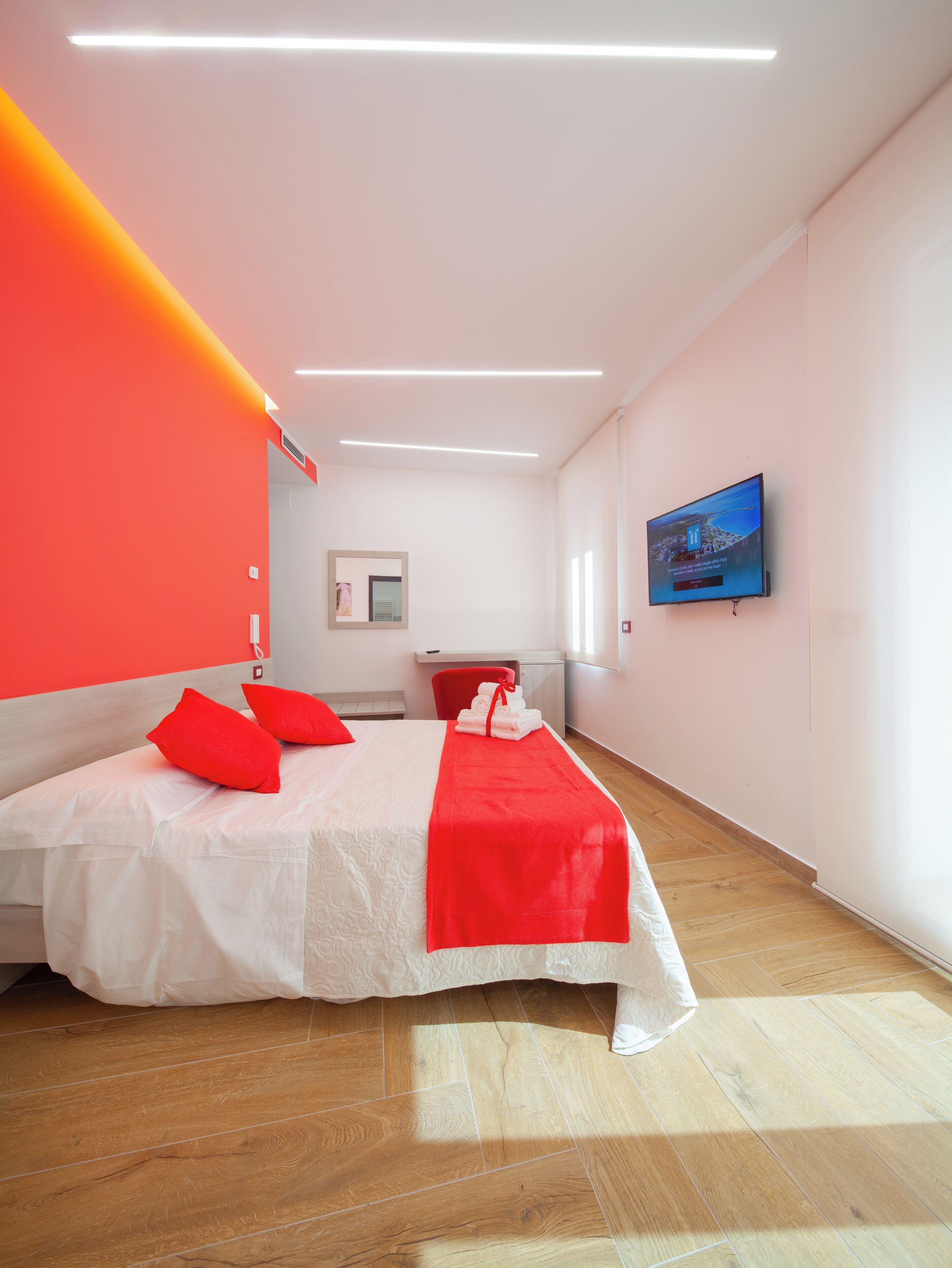 Una habitación de hotel con una cama, almohadas rojas, una toalla roja, un televisor y un espejo.