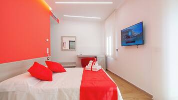 Una habitación de hotel con una cama, almohadas rojas, una toalla roja, un televisor y un espejo.