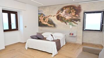 Une chambre avec une grande fresque murale, un lit recouvert de draps blancs, un plancher en bois et une fenêtre donnant sur un paysage.