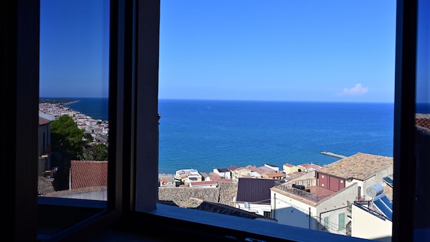Paisaje costero urbano a través de una ventana, con edificios, cielo azul despejado y el mar.