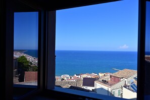 Paisaje costero urbano a través de una ventana, con edificios, cielo azul despejado y el mar.