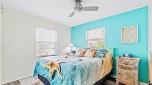 A bedroom with a bed, a ceiling fan, a nightstand, and a wall with a framed quote.