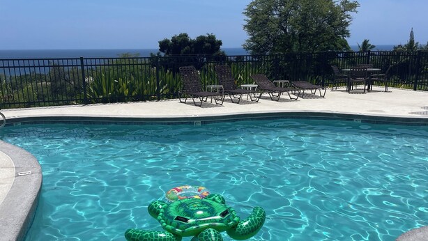 A clear blue pool with a green inflatable turtle float, surrounded by lounge chairs and a view of the ocean. - New updated 2-bedroom condo! Absolutely no stairs! Ocean and golf course views! (Kailua-Kona)
