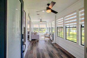 A spacious hallway with a ceiling fan, large windows, and a seating area with a sofa and chairs. - Woodsy Lakehouse Getaway (Huffman)