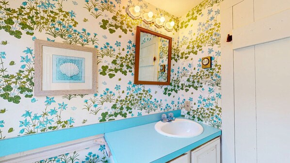 Un bagno con carta da parati a motivi floreali, un quadro incorniciato, uno specchio e un lavandino blu.