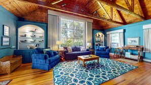 Ein gemütliches Wohnzimmer mit Holzdielen, blauen Sofas und einem gemusterten Teppich.