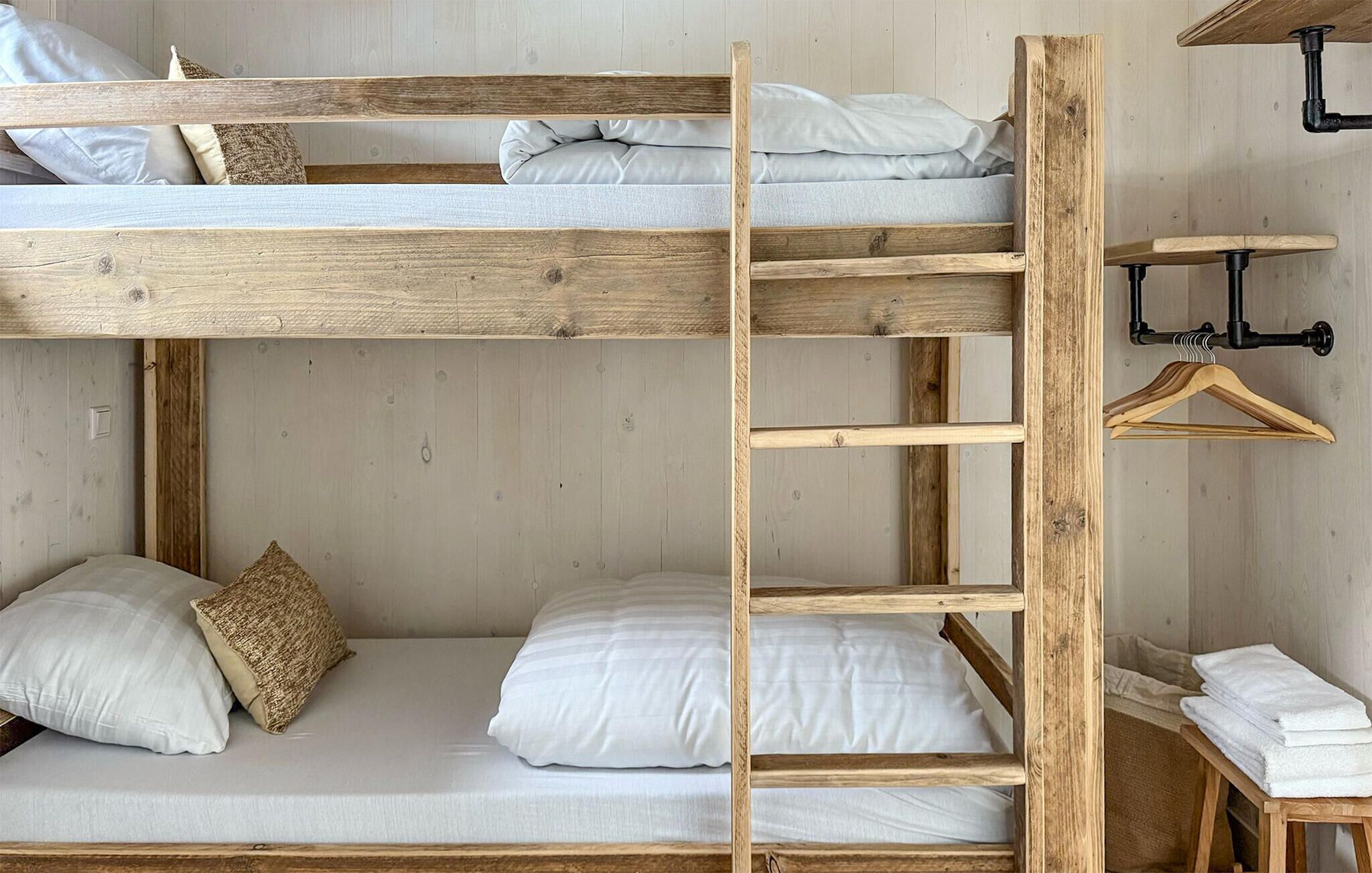 Una cama litera con escalera de madera, ropa de cama blanca y una pequeña mesa de madera con toallas.