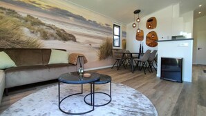 A modern living room with a beach mural, a round coffee table, and a dining area with chairs.
