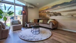 A modern living room with a large window, a round coffee table, a sofa, and a mural on the wall.