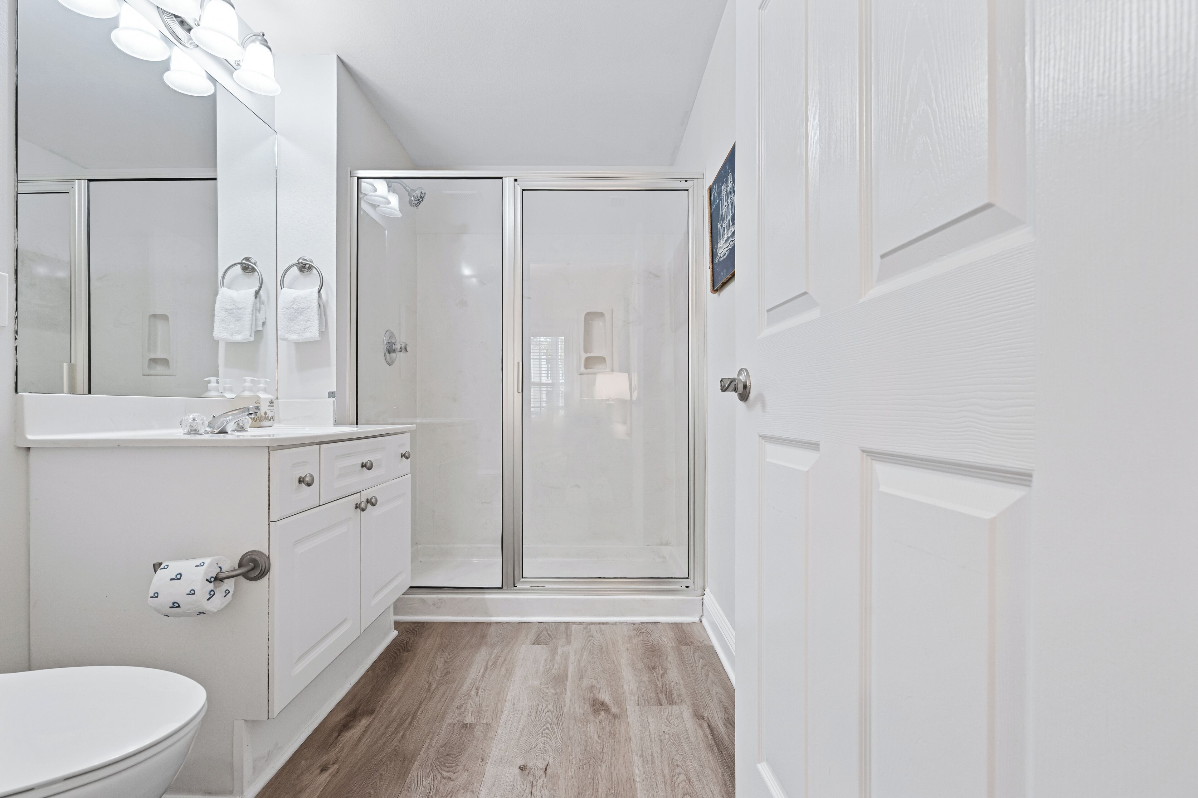 A modern bathroom with a white vanity, a glass shower enclosure, and a large mirror with lights.