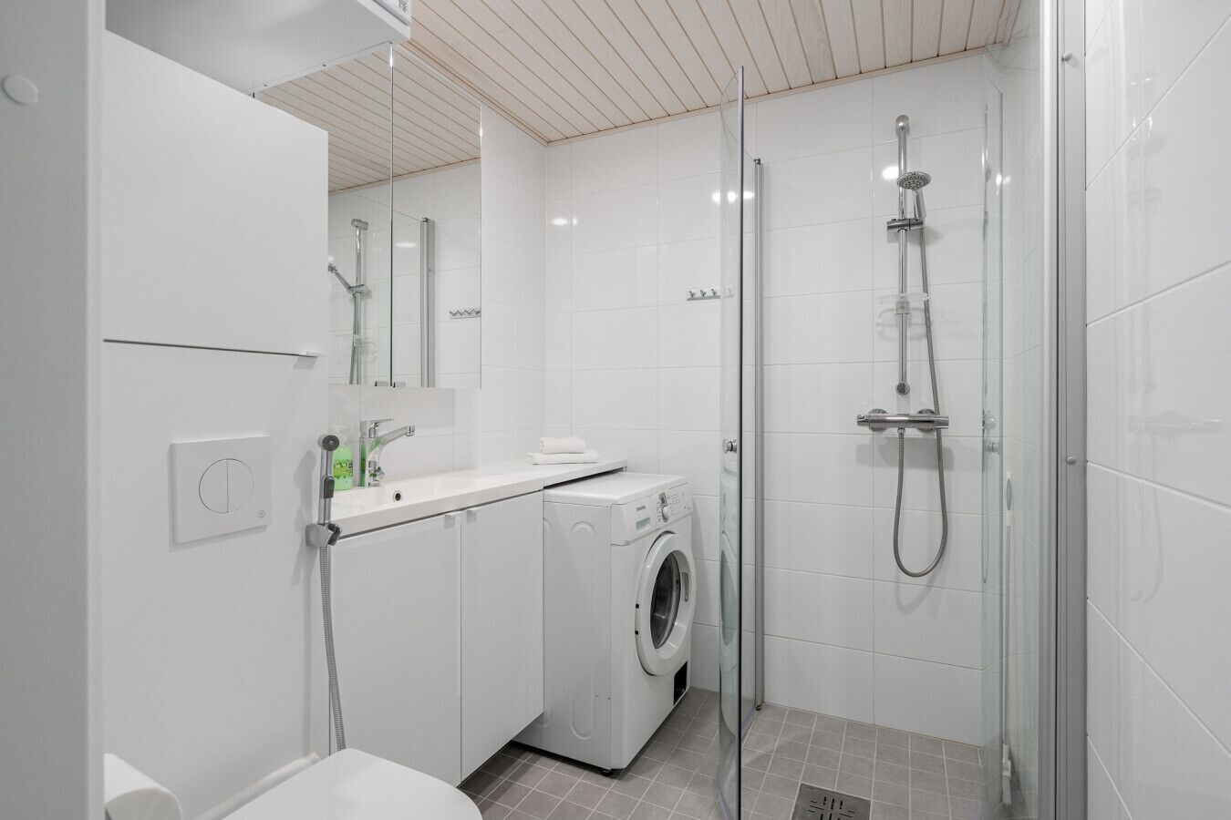 A modern bathroom with a glass shower enclosure, a built-in washing machine, and a white sink with a mirror above it.