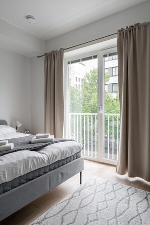 Et moderne soveværelse med en seng, et natbord, en lampe og udsigt til en balkon med gardiner.