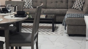 A living room with a sofa, coffee table, and dining area with chairs and a table set for two.