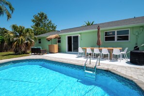 A swimming pool with a ladder, surrounded by a patio area with outdoor furniture and a table.