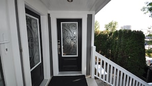 A front door with decorative glass panels, a black doormat, and a white railing.