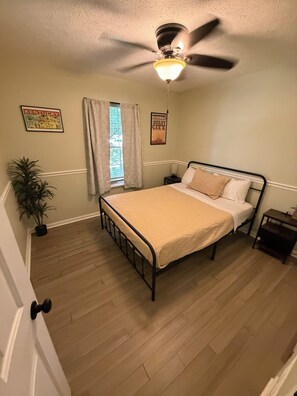 A bedroom with a bed, a ceiling fan, a window with curtains, and two wall decorations. - Modern Comfort 
•Bourbon Trail & Derby•Fenced yard•full kitchen•parking (Shepherdsville)