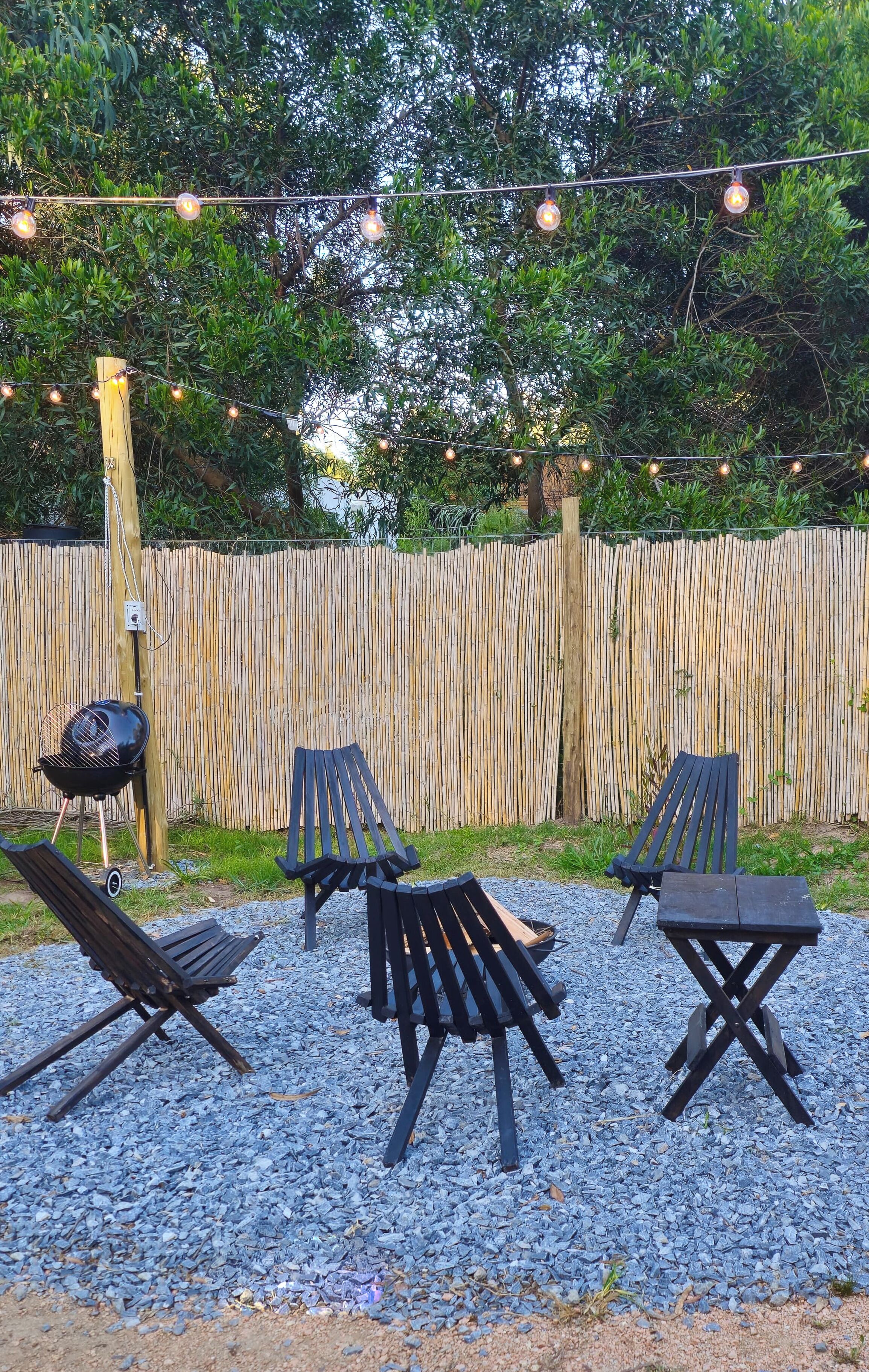 Un espace extérieur aménagé avec des chaises et une table, un barbecue et une clôture en bambou.