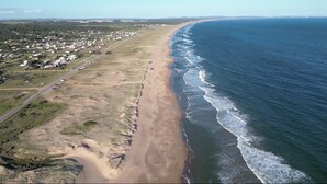 Luchtbeeld van een kustgebied met een strand, een weg en een woongebied.
