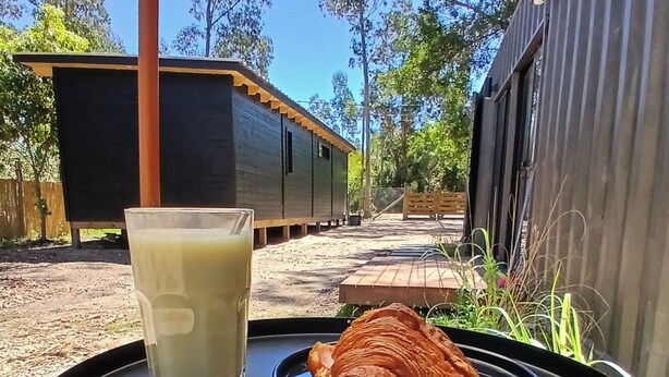 Een tafel met een glas ijsthee en een croissant op een houten terras.