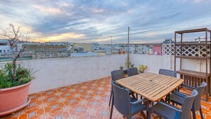 Terrassa al terrat amb taula i cadires de fusta, plantes en testos i vista panoràmica de la ciutat.