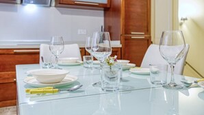 Taula de menjador coberta amb vidre transparent, plats i un ram de flors, en una cuina moderna amb armaris de fusta i un taulell de vidre.
