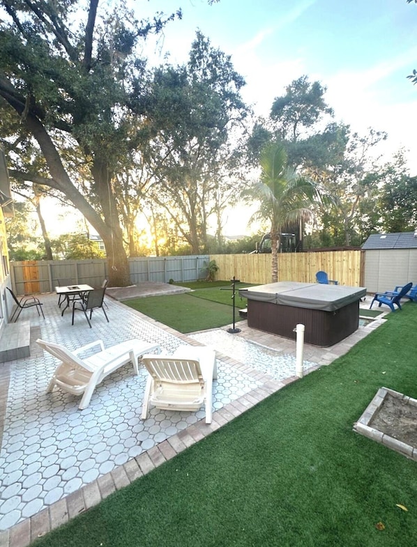 A backyard patio with hexagonal tiles, a hot tub, and a small lawn area.