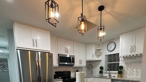 A modern kitchen with white cabinets, stainless steel appliances, a granite countertop, and bar stools.