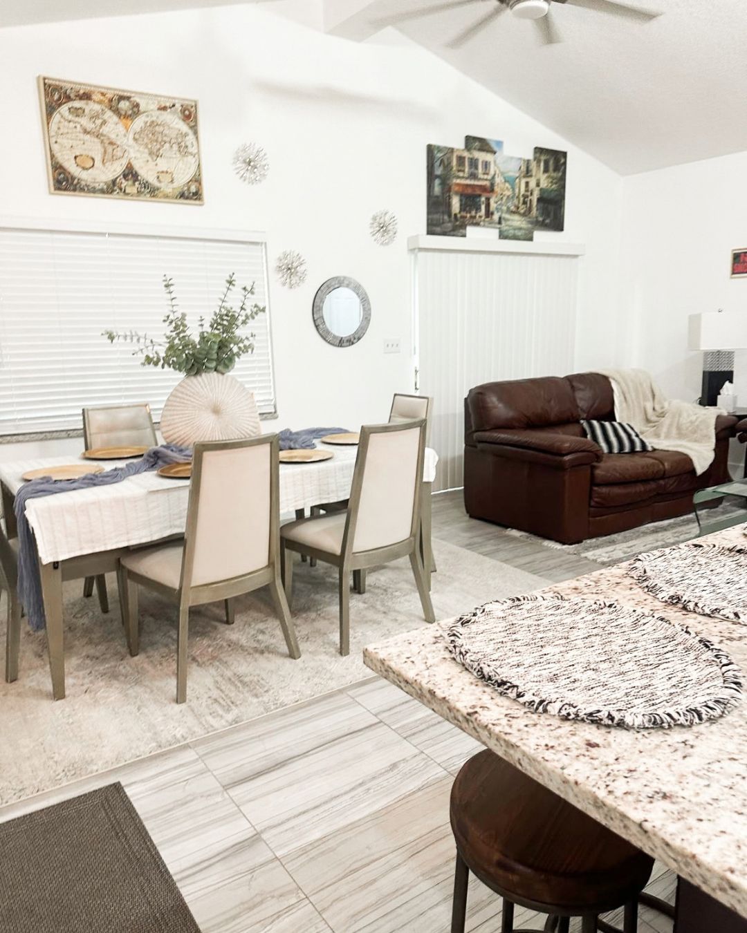 A dining area with a table set for four, a brown leather sofa, and a ceiling fan.