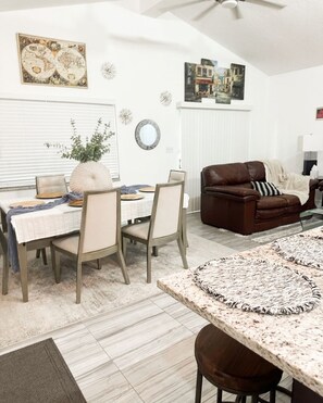 A dining area with a table set for four, a brown leather sofa, and a ceiling fan. - Lovely 2-bedroom house in Howey-in-the-Hills (HOWEY-IN-THE-HILLS)